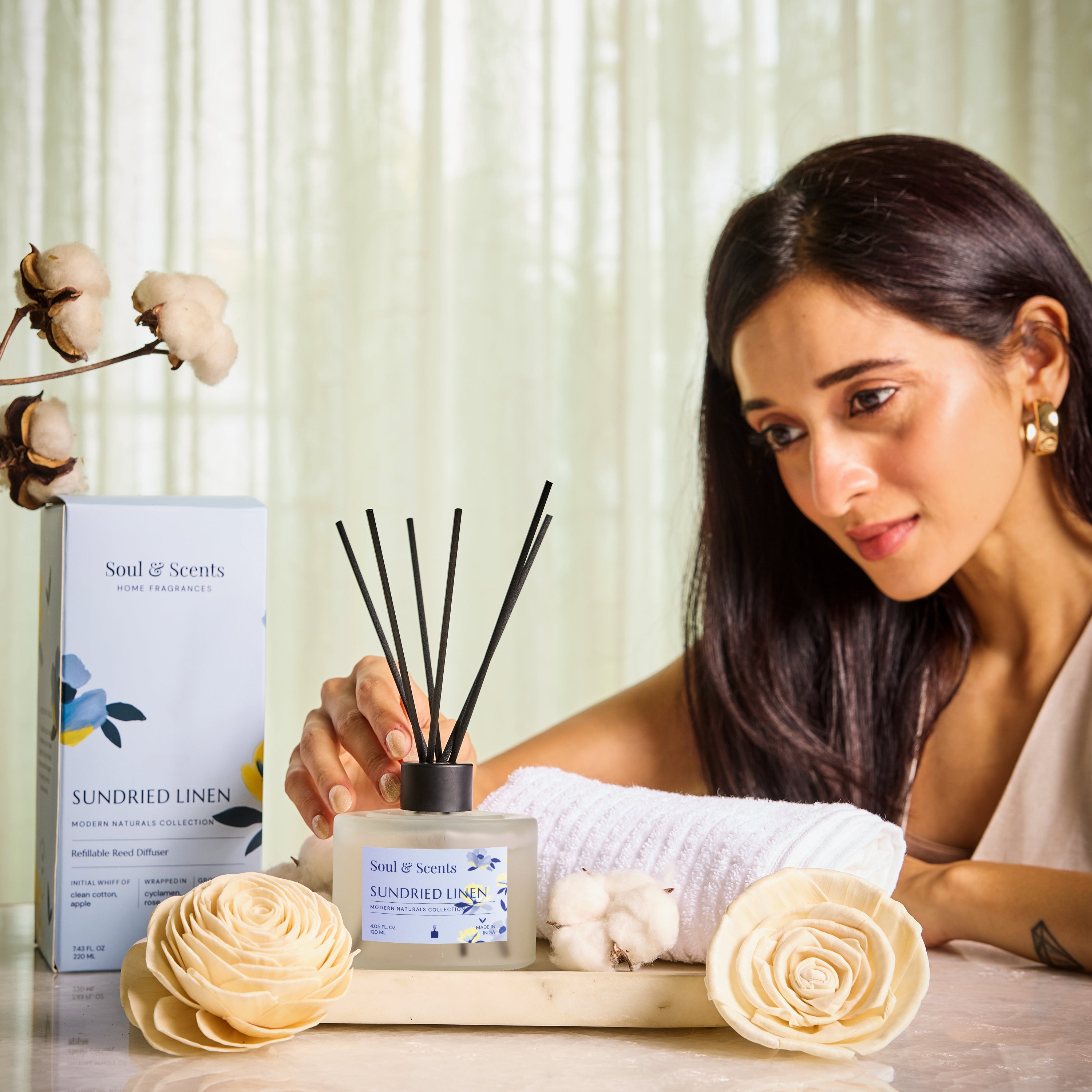 Woman holding a diffuser with 'Soul & Scents' packaging, surrounded by decorative items on a table.