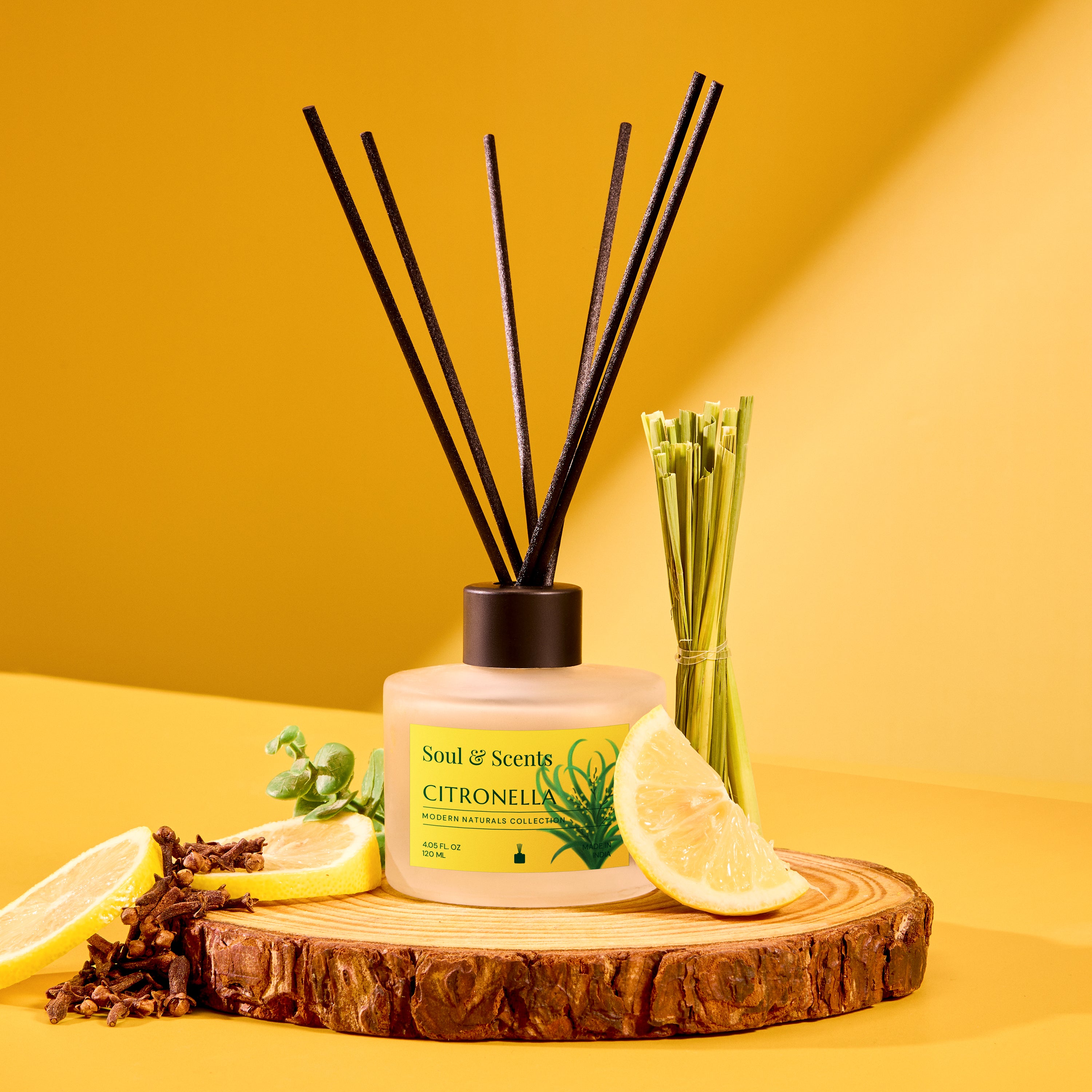 Scented diffuser with citronella label on a wooden platform with lemons and herbs against a yellow background