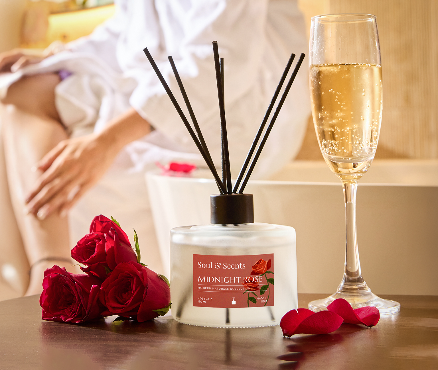 Scented diffuser with 'Midnight Rose' label, red roses, and a glass of champagne on a table.