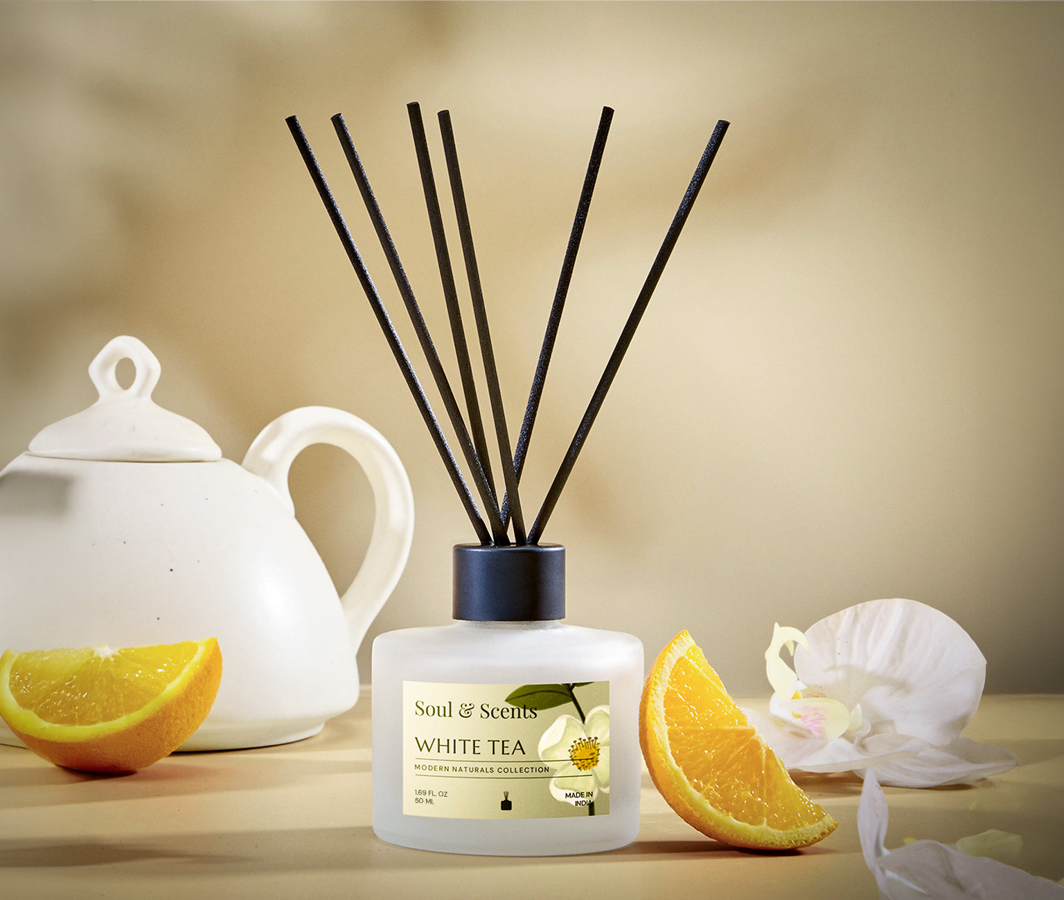 Scented diffuser with reeds, a teapot, and oranges on a wooden surface.