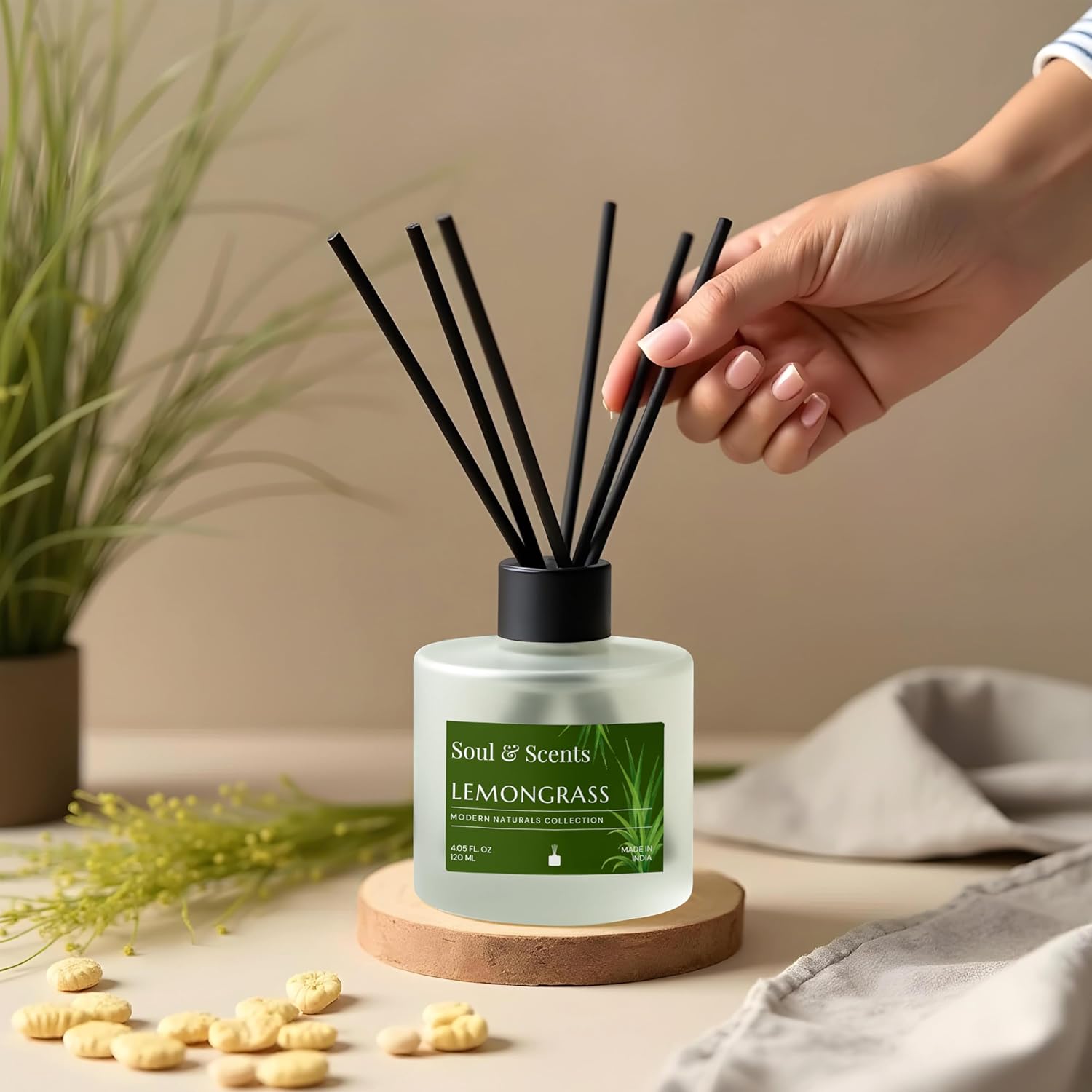 Soul & Scents Lemongrass diffuser with hand holding black sticks, plant and towel in background