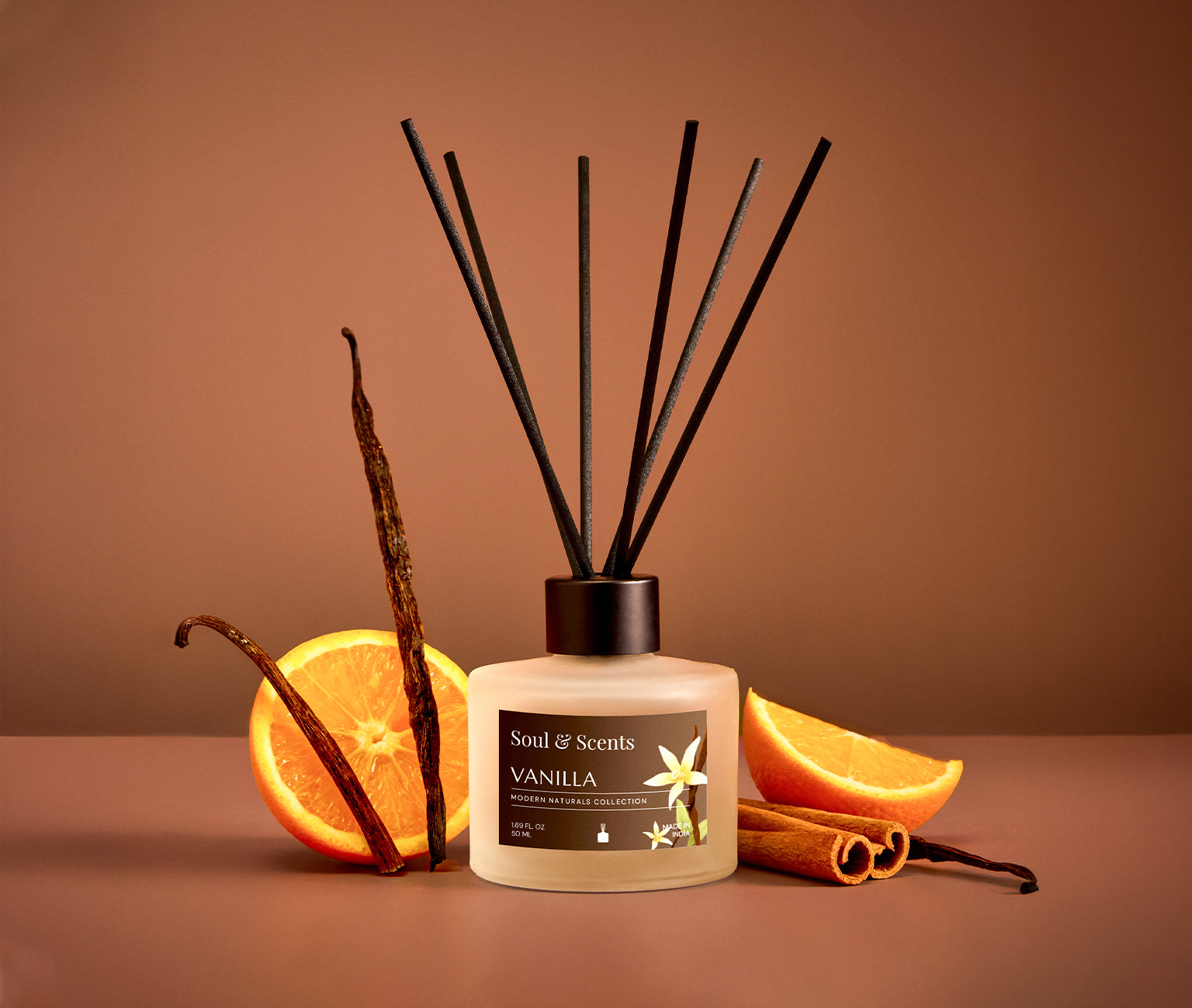 Vanilla-scented diffuser with vanilla beans, oranges, and cinnamon sticks on a brown background