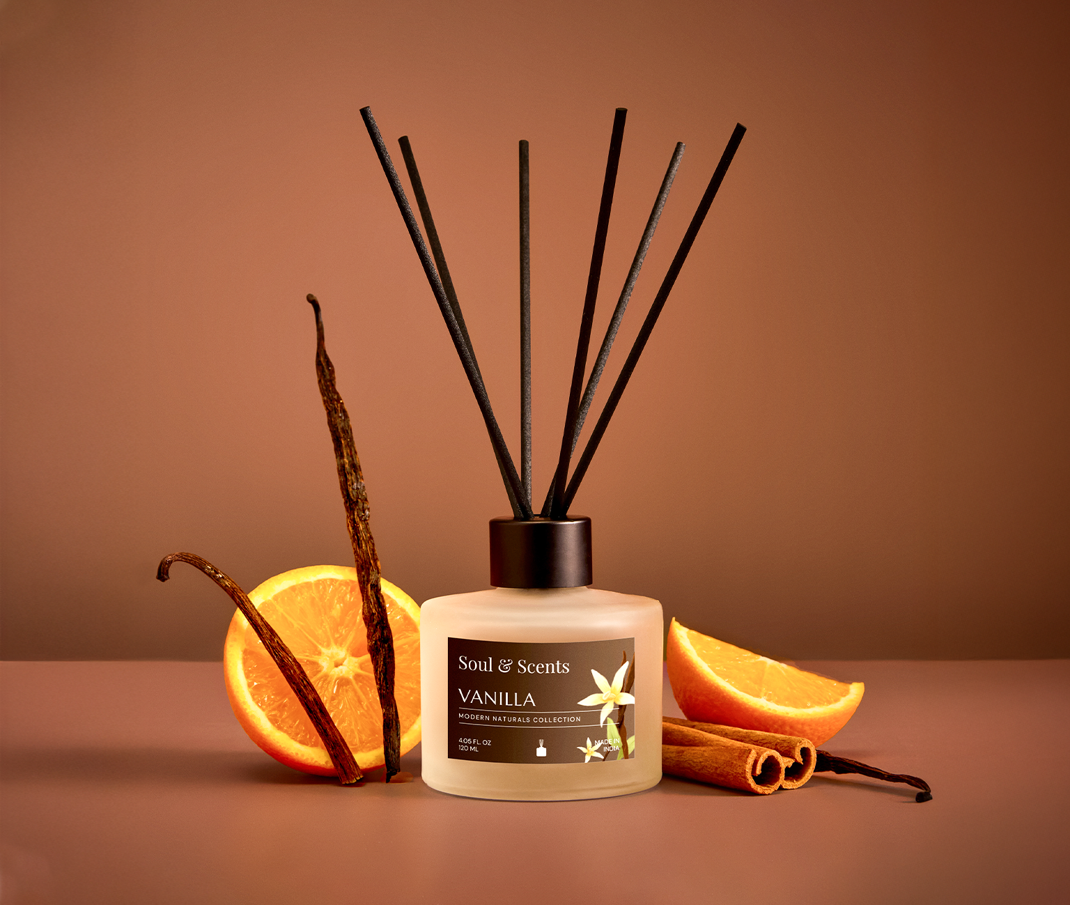 Vanilla-scented diffuser with vanilla beans, oranges, and cinnamon sticks on a brown background