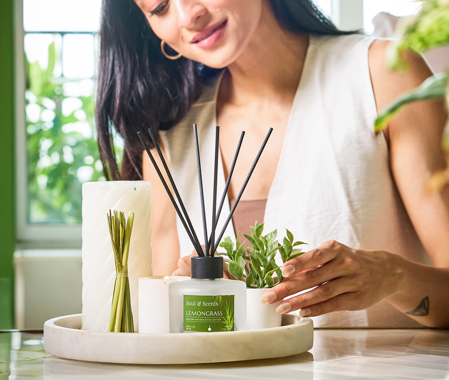 Woman interacting with a diffuser and plants on a table, with a blurred indoor background.
